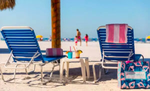 Two empty beach chairs on the beach. Two colorful cocktails are on the chair between them.