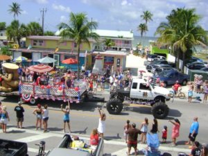 Yucatan Beach Stand's float in the Fort Myers Beach Fourth of July Parade. Its a red white and blue themed float pulled by a white monster truck. A giant tiki is riding on the float.