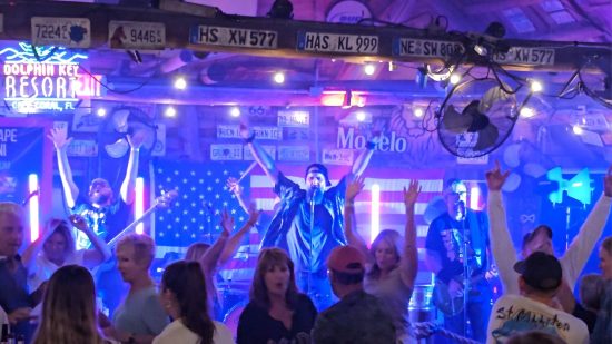 Live band at Dolphin Key Resort with dancing crowd, string lights, and license plates overhead.