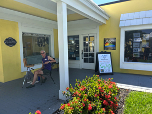 Artist painting outside Fort Myers Beach Art Association Gallery, near signs for Eyes Etc Optical and Spring Fling.