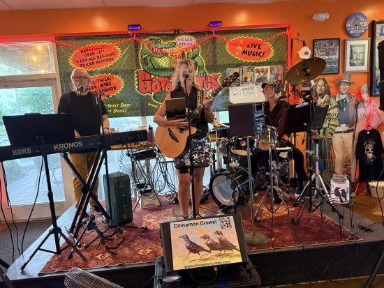 Cinnamon Crows band performing live at Gator Bites with colorful backdrop and happy hour signage.