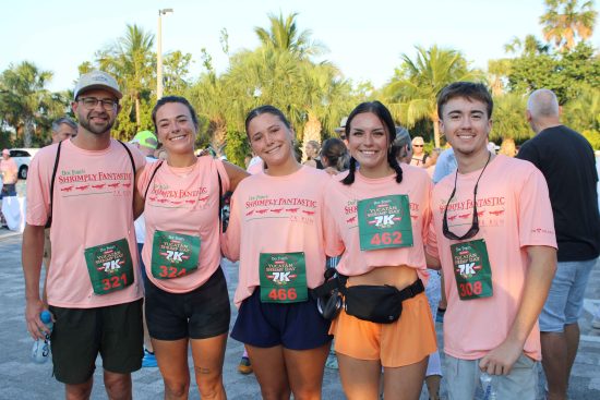 Group of five runners in pink Doc Ford’s 7K shirts posing together outdoors before the race.