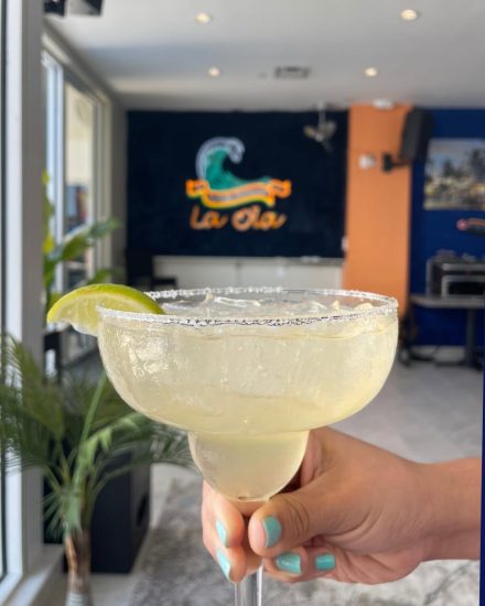A salted-rim margarita with a lime wedge held up inside La Ola Surfside restaurant.