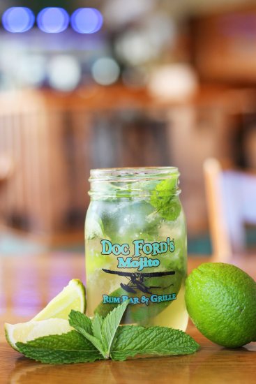 Mojito cocktail in Doc Ford's branded mason jar with fresh lime wedges and mint leaves on wooden bar counter.