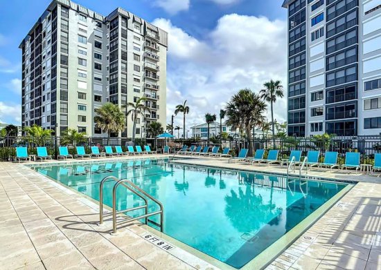 Swimming pool with blue lounge chairs and palm trees at modern apartment complex with high-rise buildings