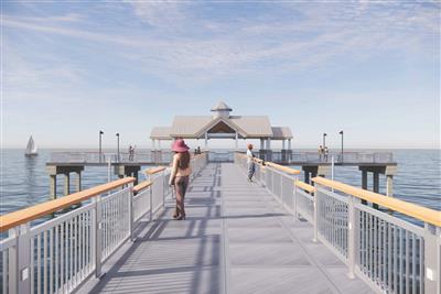 Pier walkway with two visitors heading to waterfront pavilion, sailboat visible on calm blue water