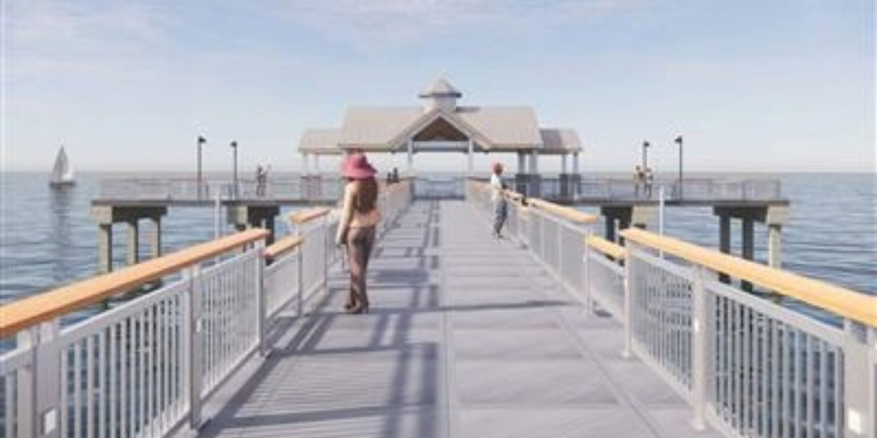 People walking on a wooden pier with white railings leading to a covered pavilion, ocean views and sailboat in distance.